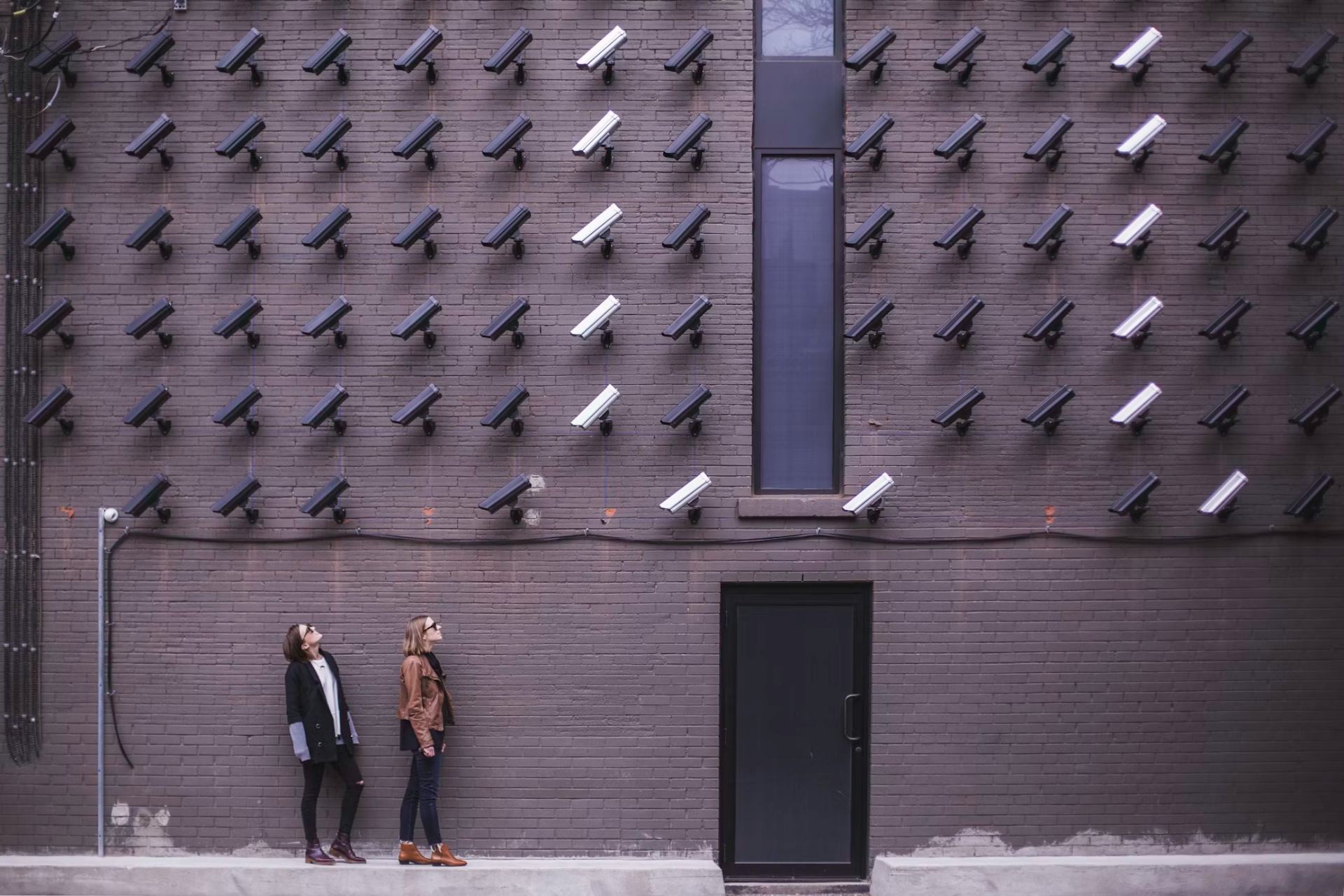 Surveillance cameras installed on wall with 2 women looking at these cameras above them